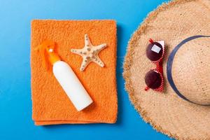 Summer beach flat lay accessories. Sunscreen bottle cream, towel and seashells on colored Background. Travel holiday concept with copy space photo