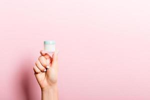 Female hand holding cream bottle of lotion isolated. Girl give jar cosmetic products on pink background photo