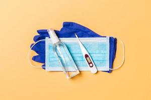 Top view of latex gloves, bottle of alcohol hand sanitizes, medical mask and digital thermometer on orange background. Antibacterial virus protection concept with copy space photo
