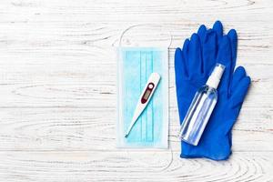 Top view of hygienic mask, latex gloves, digital thermometer and alcohol gel sanitizer on wooden background. Protective equipment concept with copy space photo