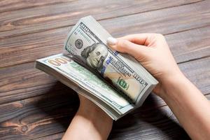 Businesswoman's hands counting one hundred dollar bills on wooden background. Salary and wage concept. Perspective view of Investment concept photo