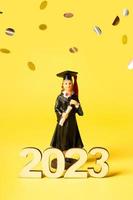 Class of 2023 concept. Wooden number 2023 with graduate statuette on color background with flying tinsel photo