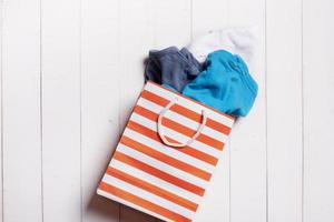 Colorful clothing and shopping paper bag on wooden background. Second hand, recycle reuse concept photo