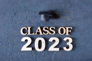 Class of 2023 concept. Wooden number 2023 with graduate hat on dark background with tinsel photo