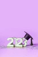 Class of 2023 concept. Wooden number 2023 with graduated cap on colored background photo