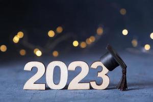 clase de 2023 concepto. de madera número 2023 con graduado sombrero en oscuro antecedentes con bokeh foto