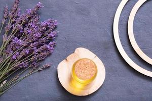 Lavender flowers and bottle with yellow oil on wooden podium on dark background. Wellness flat lay concept photo