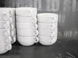 White coffee or tea cups in a row on the bar counter. A stack of empty dishes photo