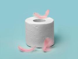 A roll of soft toilet paper on a blue background and delicate pink feathers photo