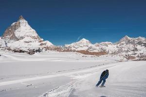 Young man skiing in Zermatt ski resort right next to the famous Matterhorn peak. Beautiful sunny day for snowboarding. Winter sports concept. photo