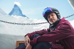 Portrait of smiling tourist snowboarder sitting inside an iglu dorf with a view on the famous snowcapped Matterhorn mountain. Relaxing in Swiss Alps, Zermatt ski resort. photo