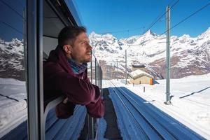 Young man riding a train of Gonergratbahn running to the Gornergrat station and Stellarium Observatory - famous touristic place with clear view to Matterhorn. Glacier Express train. photo