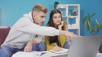 Università studenti seduta insieme a tavolo e utilizzando il computer portatile. giovane uomo e ragazza studiando insieme a casa, guardare a il computer portatile. video