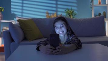 contento joven mujer utilizando teléfono inteligente, hojeada social medios de comunicación, comprobación noticias, enviar mensajes de texto joven mujer sonriente, disfrutando utilizando móvil aplicaciones para compras, teniendo divertido, chateando en social medios de comunicación a hogar. video