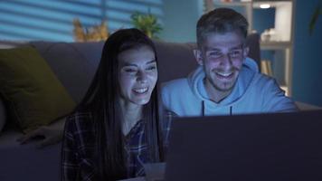 Beautiful young girl and handsome man are relaxing at night while watching movie at home. Happy young couple watching movie on laptop. Series and movie platform, home theater. video