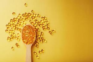 Vitamin D3 Capsules in a spoon with other vitamin D3 capsules around them on a yellow background photo