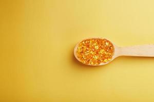 Vitamin D3 Capsules in a spoon with other vitamin D3 capsules around them on a yellow background photo