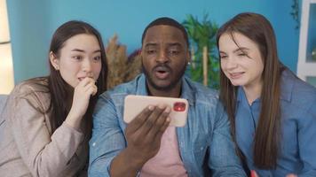 Young people of different ethnicities looking at the phone at home. They rejoice. At home, the young people look at the phone with curiosity and suddenly rejoice. video