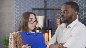 Close-up of multiethnic colleagues working together in office. Black businessman and young Asian woman taking notes, consulting each other, brainstorming while talking. video