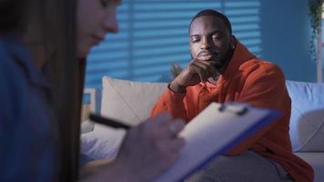 Young black man sitting in psychologist's office talking about his problems and behavior to psychiatrist woman. video