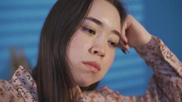 Unhappy depressed Asian young woman is overwhelmed and thinking. Young asian woman sitting alone on sofa at home thinking thoughtfully of her grief, thinking about realizing her mistake. video