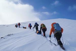 Group of mountain climbers climb the slope to the peak in sunny weather with sledges and tents equipment for overnight stays photo