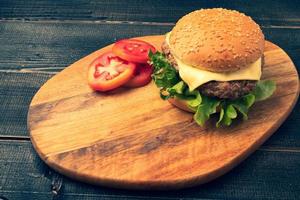 fresh tasty homemade hamburger with fresh vegetables, lettuce, tomato, cheese beside sliced tomatoes on a cutting board. Free space for text photo