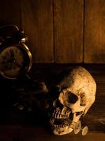 The skull is placed on a wooden table, The back of skull is drug and clock. With candles light from the sides and a wooden background. photo
