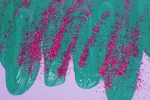 On a pink background, there are blue iridescent smudges of flowing acrylic paint with pink sparkles. photo