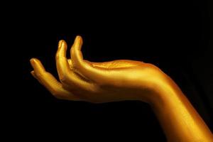 Golden female hand on a black background. Beautiful fingers covered in gold. photo