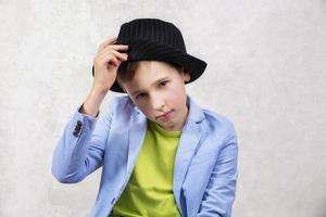 un elegante chico en un traje y un negro sombrero mira a el cámara. foto