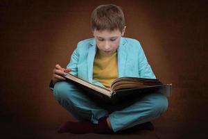 A boy in a suit sits with a book on a brown background. photo