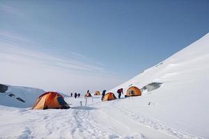 Group of mountain climbers climb the slope to the peak in sunny weather with sledges and tents equipment for overnight stays photo