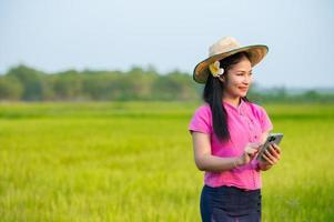 Asian female farmer holding tablet walking in rice field to store information photo