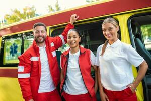 paramédicos y médico en pie en el lado ambulancia. médico es que lleva un médico trauma bolsa. grupo de Tres paramédicos en pie en frente de ambulancia con sonrisa. foto