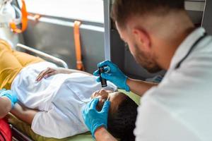 Close-up Portrait Shot of a Serious and Focused Paramedic in an Ambulance Vehicle with an Injured Patient. Emergency Medical Technician Uses Stethoscope to Monitor the Condition photo