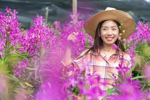 joven hembra jardineros vestir un tartán camisa y vestir un sombrero. manos participación tijeras para corte orquídeas y sonrisa. nuevo Generacion agricultor, jardineros concepto. foto