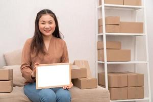 Happy young entrepreneur, sitting on the sofa and holding blank board for text and information. Concept of small business owner and Space for advertisement. photo