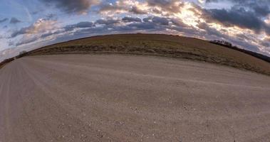 tiny planet transformation with curvature of space among fields on gravel road in evening with sky and fluffy clouds video