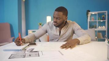 afrikanisch Mann Arbeiten auf architektonisch Projekt. Zuhause Büro arbeiten. afrikanisch Mann Arbeiten auf architektonisch Projekt allein beim heim. video