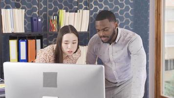 Asian woman and African man working together in the office. Asian woman and African man are working on computer in office. video