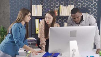 Office workers of different races work together in the office. African man, Asian and European woman working together in office. They are looking at the computer screen and talking. video