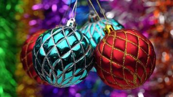 Group of cyan and red Christmas balls hanging and spinning on blurry colored bokeh background of shining tinsel, holiday lights. Closeup view of holiday toys. Soft and selective focus on foreground video