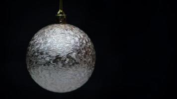 Beautiful shining Christmas ball silver color hanging and spinning on black background with copy space. Closeup of single holiday New Year's ball. Motion blur. Soft and selective focus on foreground