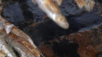 Cooking frying and stirring capelin fish fried in black pan. Close-up view of chef stirs roasted caplin fish with wooden spatula. Broiled fish - traditional Asian dish as an appetizer or garnish video