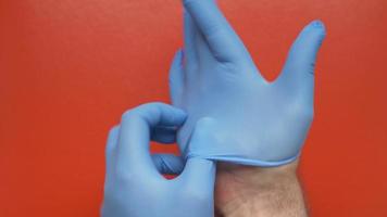 médico colocar em azul estéril cirúrgico luvas em mãos em vermelho fundo. fechar-se visualizar. conceito pandemia seguro coronavírus, higiene, protegendo mãos, vírus infecção ao controle video