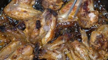 Cooking frying chicken wings in pan with oil. Close-up view of hands chef stirring roasted chicken with metal fork. video