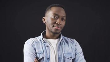 Stylish and handsome African young man with folded arms looking at camera freely and confidently. African handsome and attractive young man posing for camera on black background. video