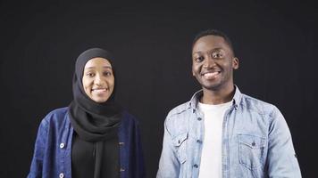 africano musulmano donna e uomo nel contento relazione guardare a telecamera e agitando contento africano musulmano coppia ridendo e Tenere mani agitando a telecamera insieme, saluto, detto ciao. video