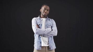 African handsome and attractive young man posing for camera on black background. Stylish and handsome African young man with folded arms looking at camera freely and confidently. video